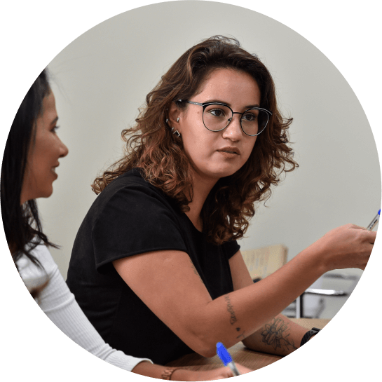 Duas mulheres, uma delas dialogando, sentadas em uma mesa